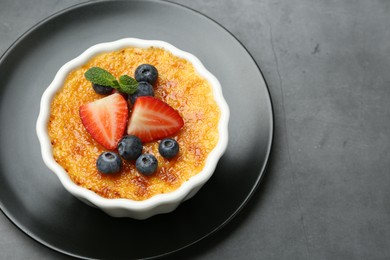 Photo of Delicious creme brulee with berries and mint in bowl on grey table, above view. Space for text