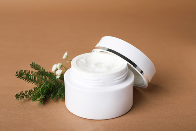 Jar of luxury face cream and plants on brown background