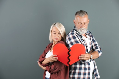 Photo of Mature couple with torn paper heart on color background. Relationship problems