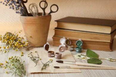 Photo of Beautiful dried flowers, books, brushes and paints on wooden table