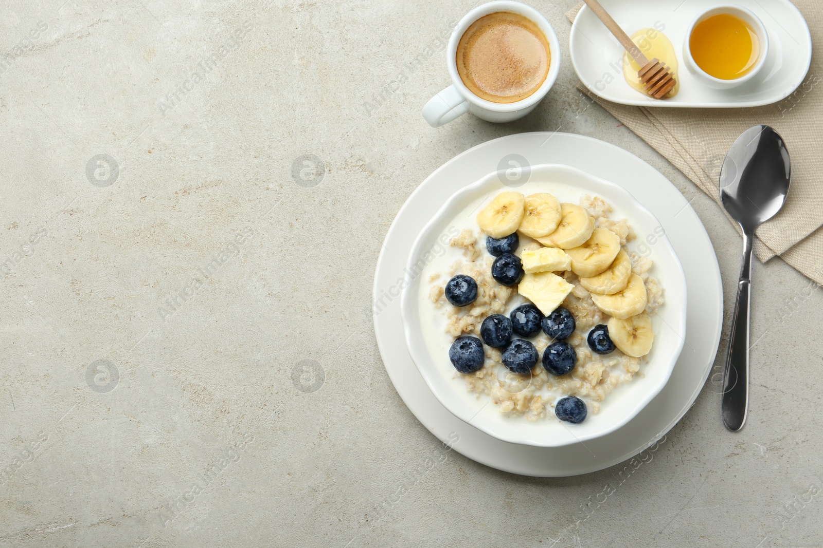 Photo of Tasty oatmeal with banana, blueberries, butter and milk served in bowl on light grey table, flat lay. Space for text