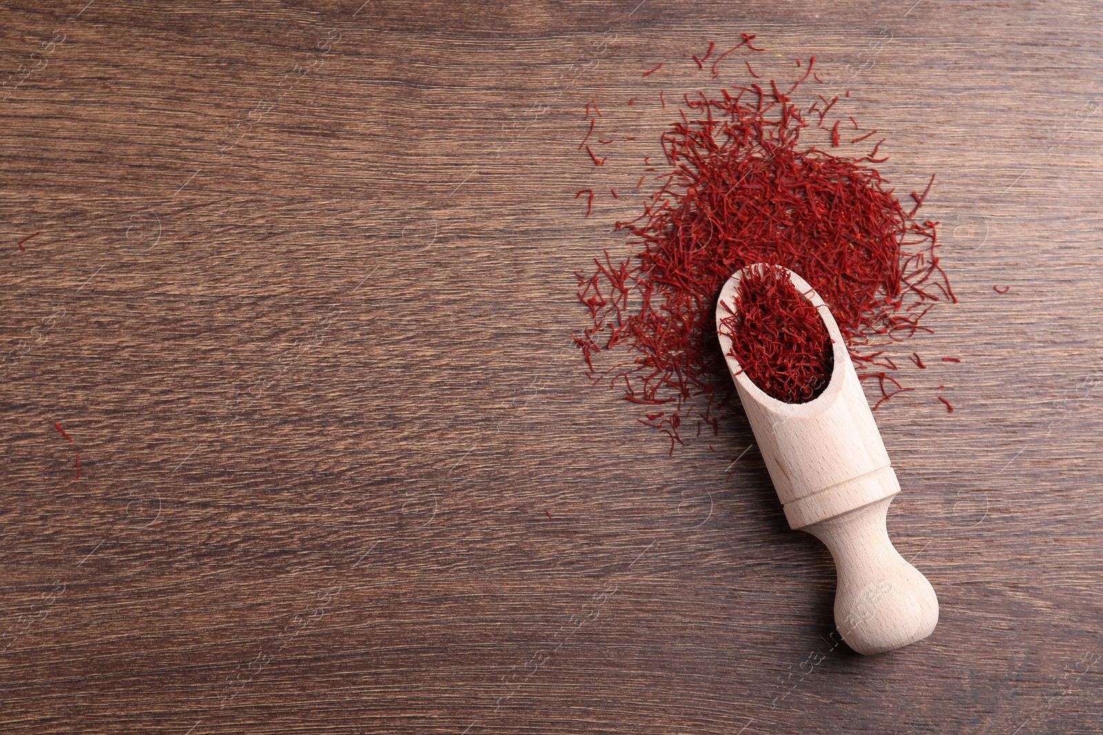 Photo of Aromatic saffron and scoop on wooden table, top view. Space for text