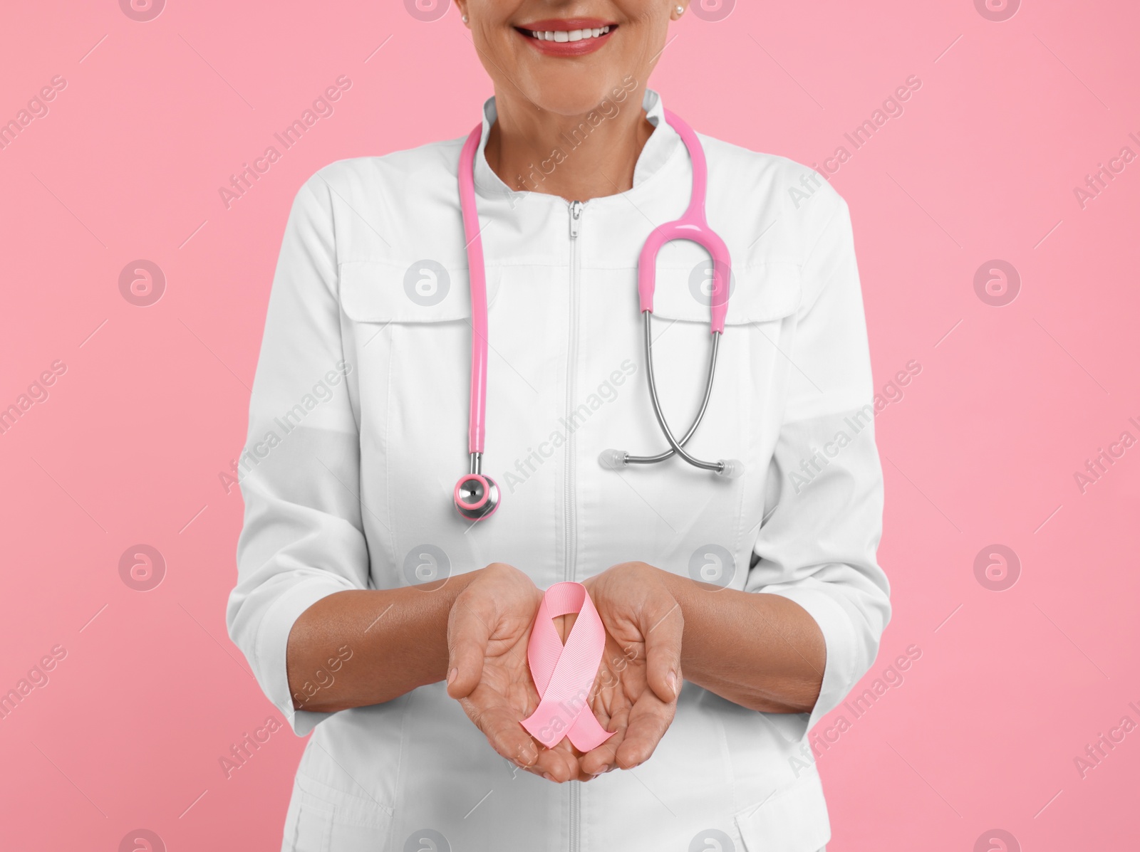 Photo of Doctor with stethoscope holding pink ribbon on color background, closeup. Breast cancer awareness