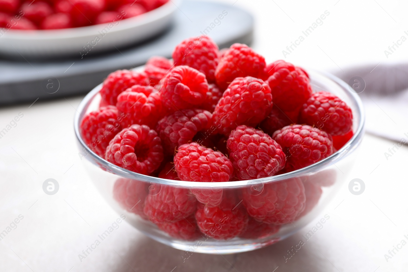 Photo of Delicious fresh ripe raspberries in glass bowl on white table, closeup