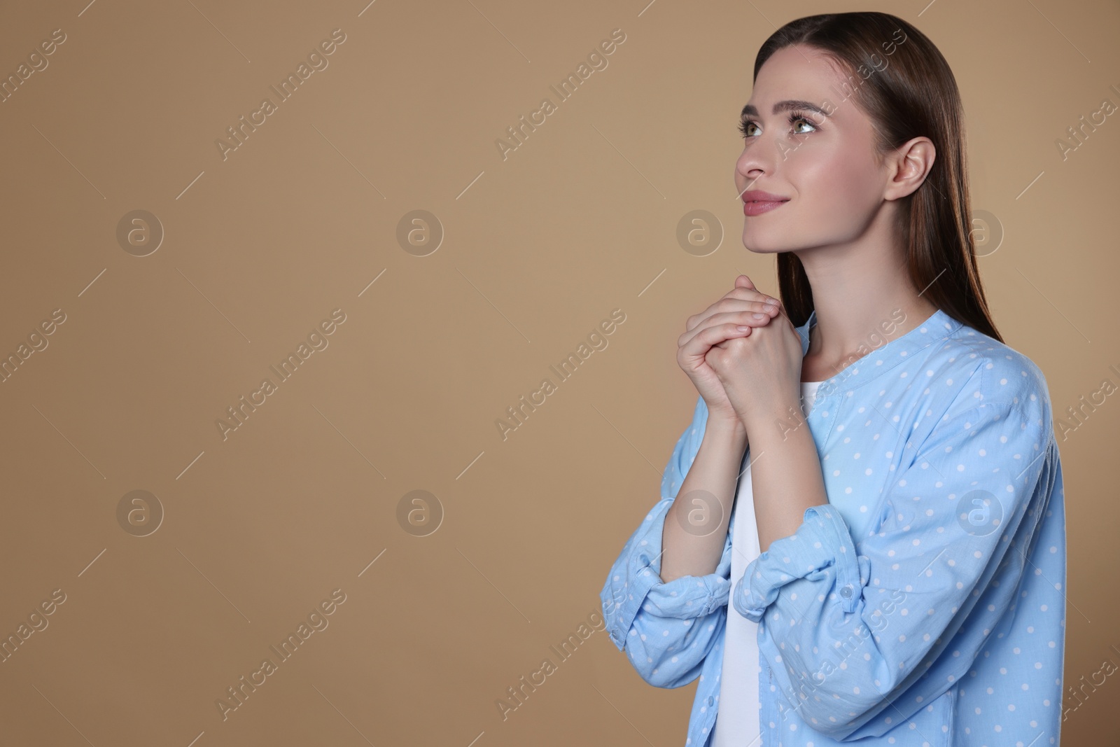 Photo of Woman with clasped hands praying on beige background, space for text