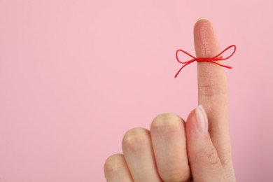 Woman showing index finger with tied red bow as reminder on pink background, closeup, Space for text