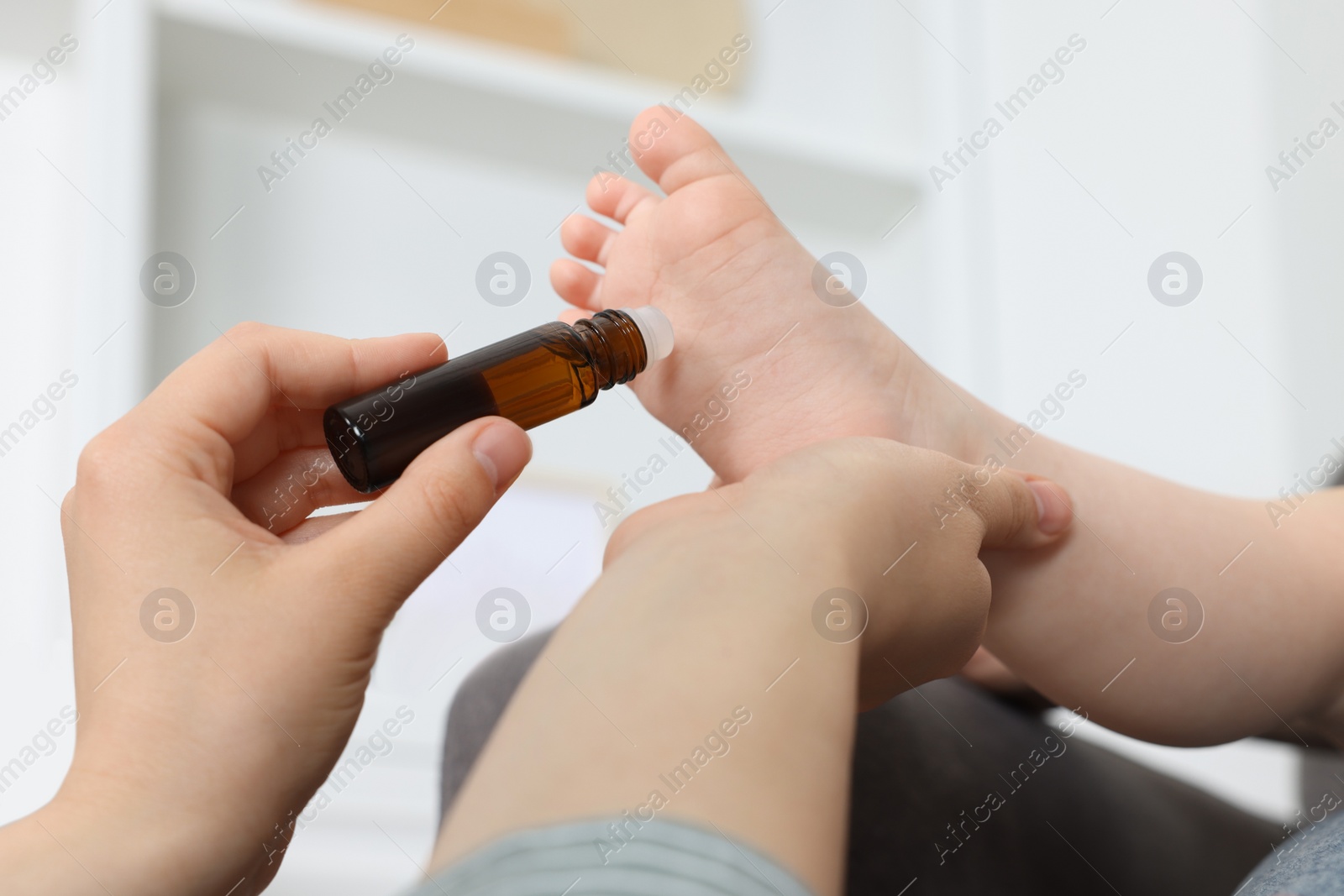 Photo of Mother applying essential oil from roller bottle onto her baby`s heel indoors, closeup