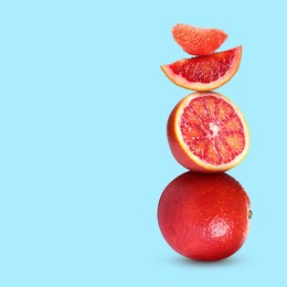 Stacked cut and whole red oranges on pale light blue background, space for text