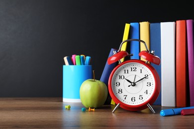 Photo of Alarm clock and different stationery on wooden table near blackboard, space for text. School time