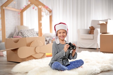 Photo of Cute little girl playing with binoculars and cardboard airplane in bedroom