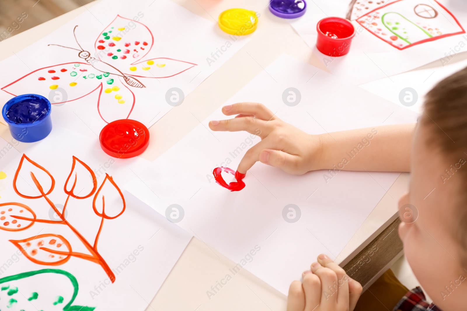 Photo of Little boy painting with finger at white table indoors, closeup