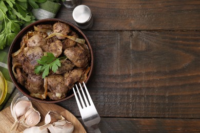 Photo of Tasty fried chicken liver with onion and parsley served on wooden table, flat lay. Space for text