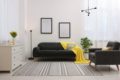 Photo of Spring atmosphere. Stylish living room interior with comfortable furniture and bouquet of beautiful yellow tulips