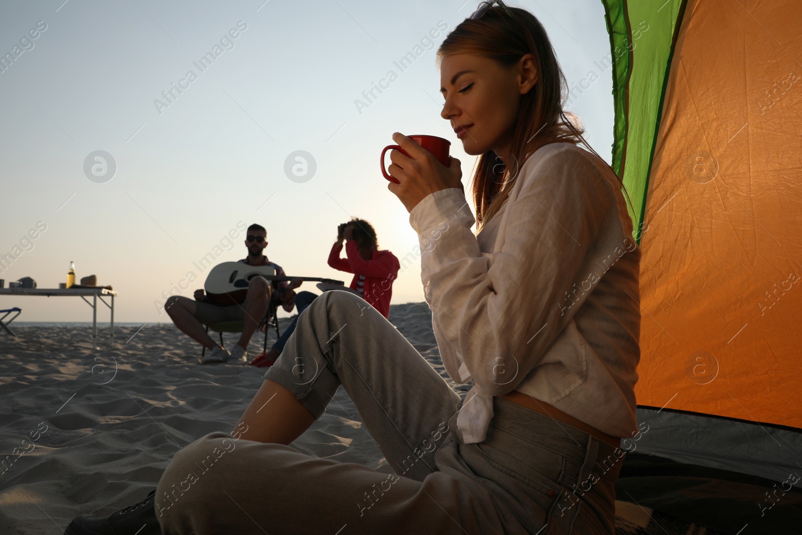 Photo of Friends resting on sandy beach. View from camping tent