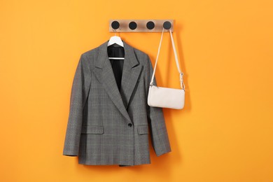 Hanger with stylish jacket and bag on orange wall