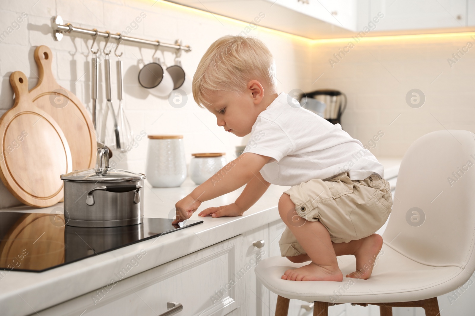 Photo of Curious little boy exploring electric stove in kitchen