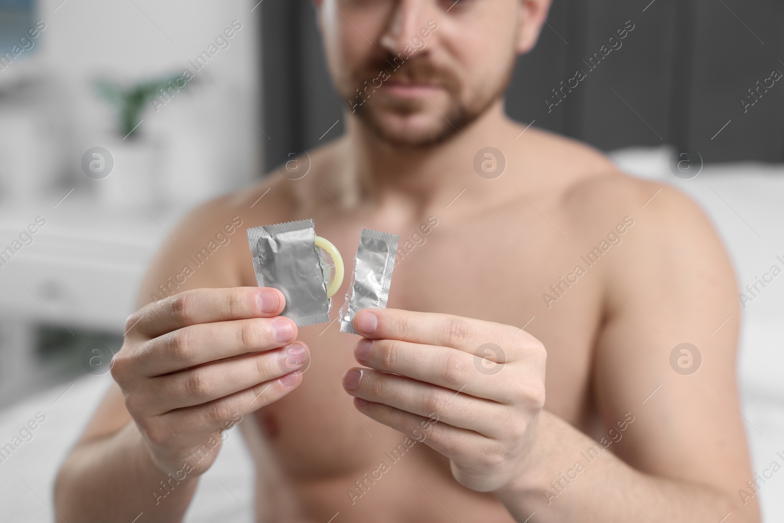 Photo of Closeup of man holding open pack and condom on bed indoors