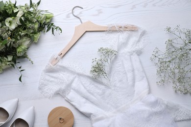 Photo of Beautiful wedding dress, engagement ring and flowers on white wooden background, flat lay