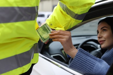 Woman putting bribe into police officer's pocket out of car window, closeup