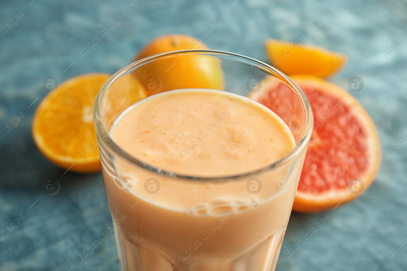 Photo of Glass with healthy detox smoothie and citrus fruits on table, closeup