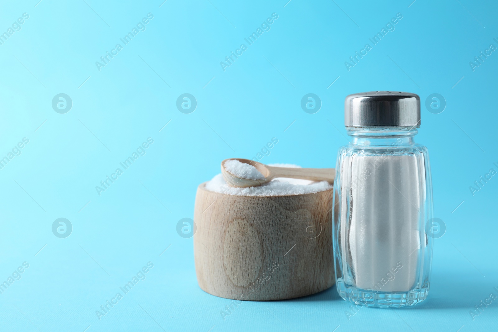 Photo of Organic white salt in bowl and shaker on light blue background, space for text