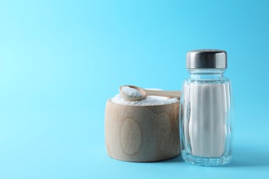 Photo of Organic white salt in bowl and shaker on light blue background, space for text