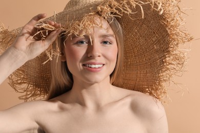 Beautiful young woman in straw hat on beige background
