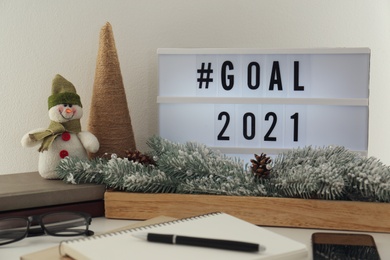 Light box with hashtag Goal 2021 near notebook on table. New year targets