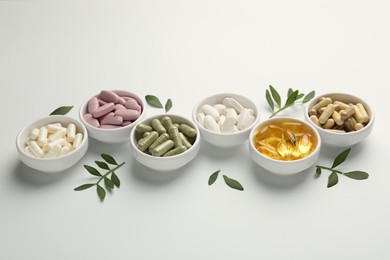 Photo of Different vitamin capsules in bowls and leaves on white background