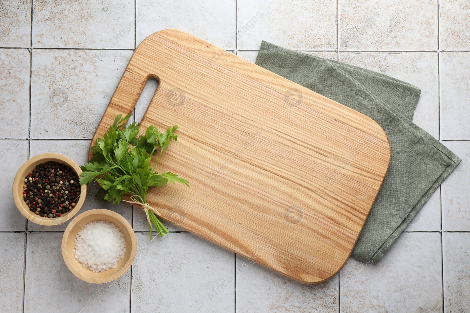 Photo of Cutting board, salt, pepper and parsley on white tiled table, flat lay. Space for text