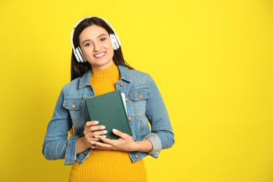 Young woman listening to audiobook on yellow background. Space for text