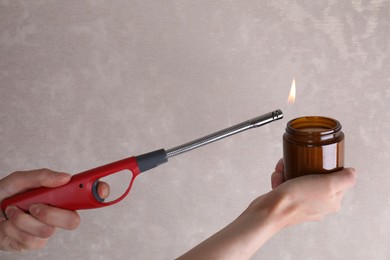 Photo of Woman lighting candle with gas lighter against grey wall, closeup