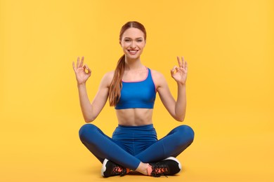 Young woman in sportswear showing OK gestures on yellow background