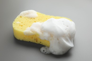 Photo of Yellow sponge with foam on grey background, closeup