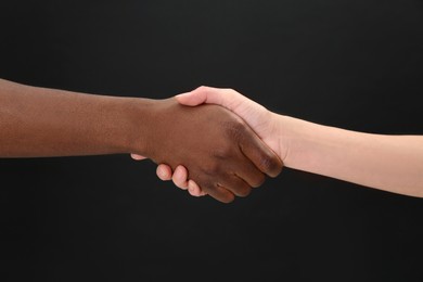 Woman and African American man shaking hands on black background, closeup