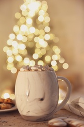 Photo of Tasty hot drink with marshmallows on table against Christmas lights. Space for text