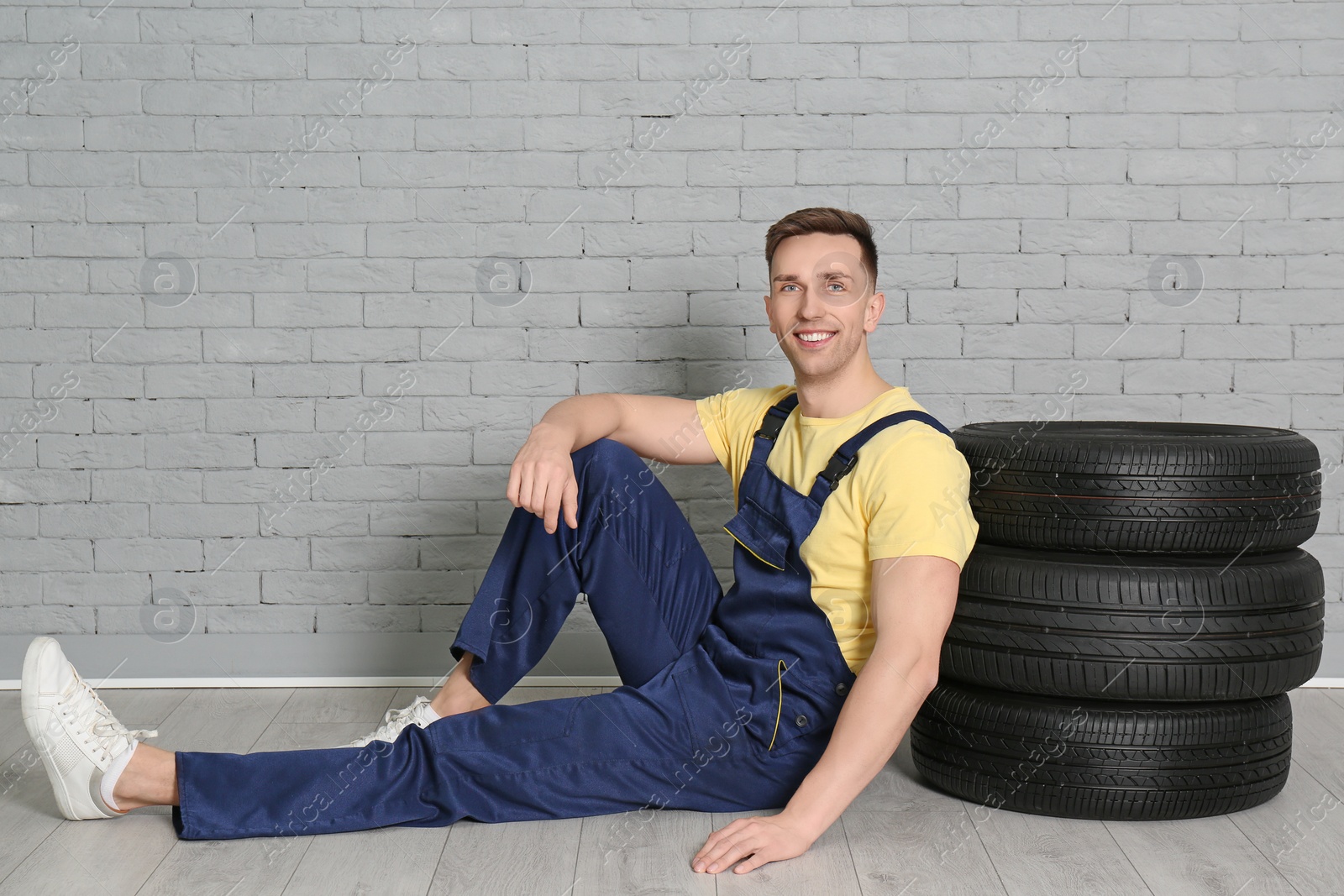 Photo of Male mechanic with car tires on brick wall background
