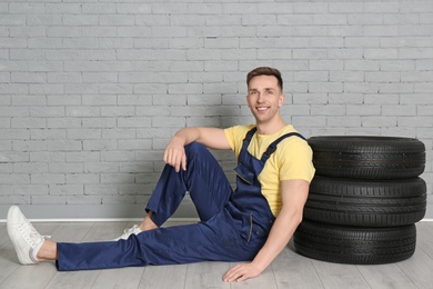 Male mechanic with car tires on brick wall background