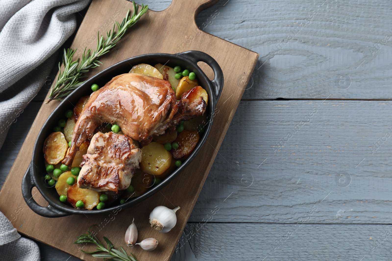 Photo of Tasty cooked rabbit with vegetables in baking dish on grey wooden table, top view. Space for text