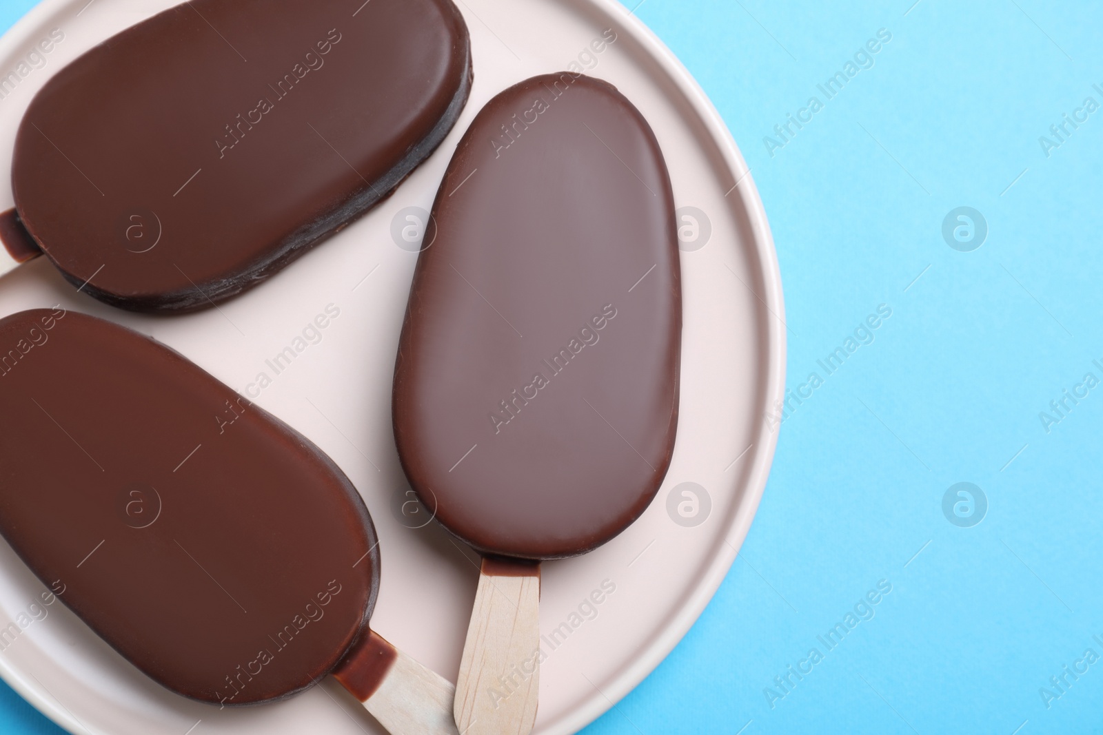 Photo of Plate with glazed ice cream bars on light blue background, top view. Space for text