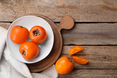 Photo of Delicious ripe persimmons on wooden table, top view. Space for text