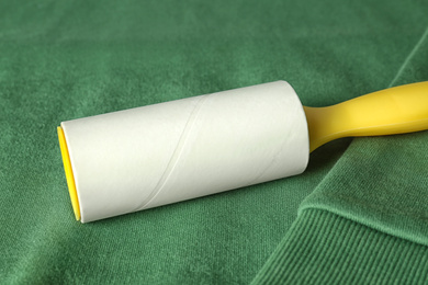 Photo of New lint roller with yellow handle on green sweatshirt, closeup
