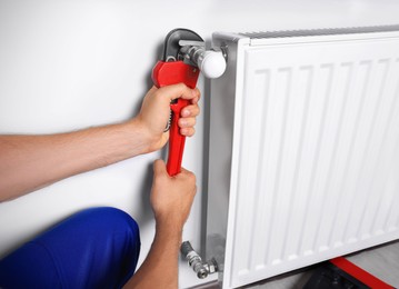 Photo of Professional plumber using adjustable wrench for installing new heating radiator indoors, closeup