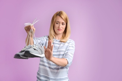 Young woman with stinky shoes on color background. Air freshener