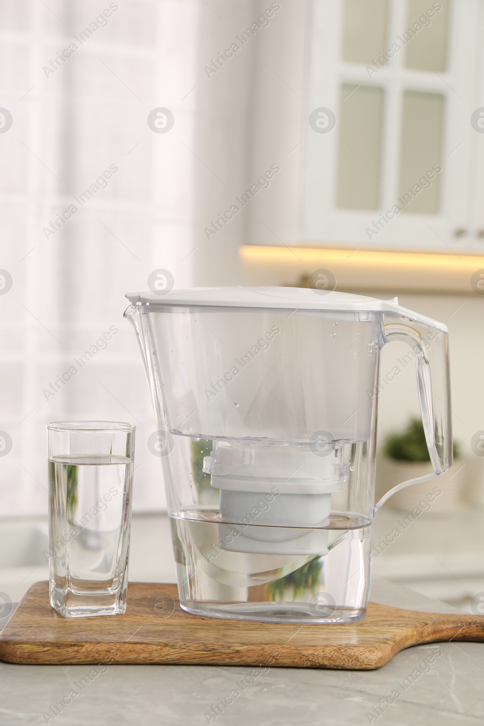 Photo of Water filter jug and glass on light table in kitchen