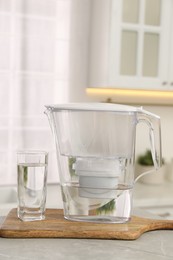 Photo of Water filter jug and glass on light table in kitchen