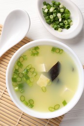 Photo of Bowl of delicious miso soup with tofu served on white wooden table, flat lay