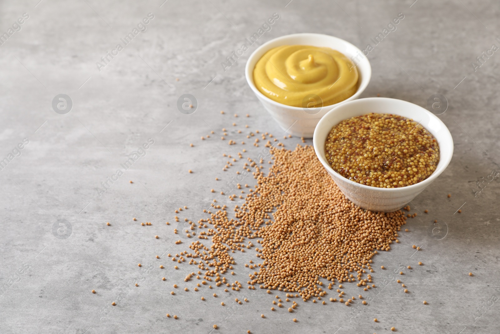 Photo of Bowls with mustard and seeds on grey table, space for text