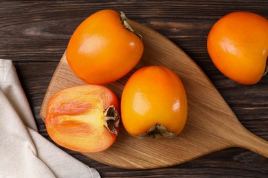 Photo of Whole and cut delicious ripe persimmons on wooden table, top view