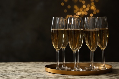 Photo of Tray with glasses of champagne on table against blurred lights. Space for text
